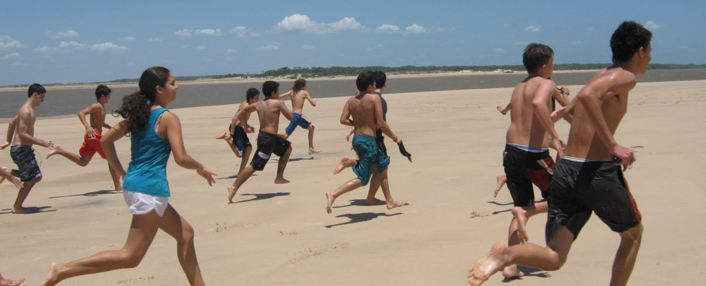 Imagem de várias crianças da Escola Vila correndo da orla da praia