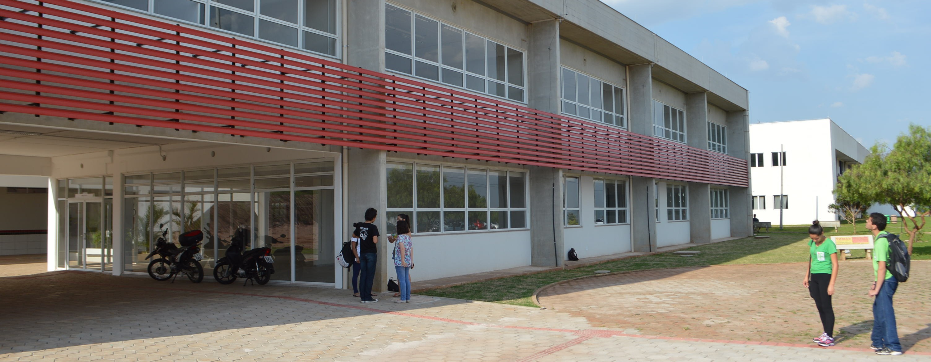 A foto mostra a fachada do IFPR: um prédio de dois andares com janelas brancas com detalhes vermelhos de metal entre elas
