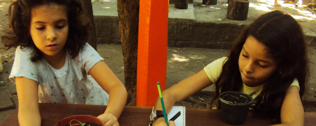 Duas crianças estão sentadas em uma mesa e desenham em folhas de papel.