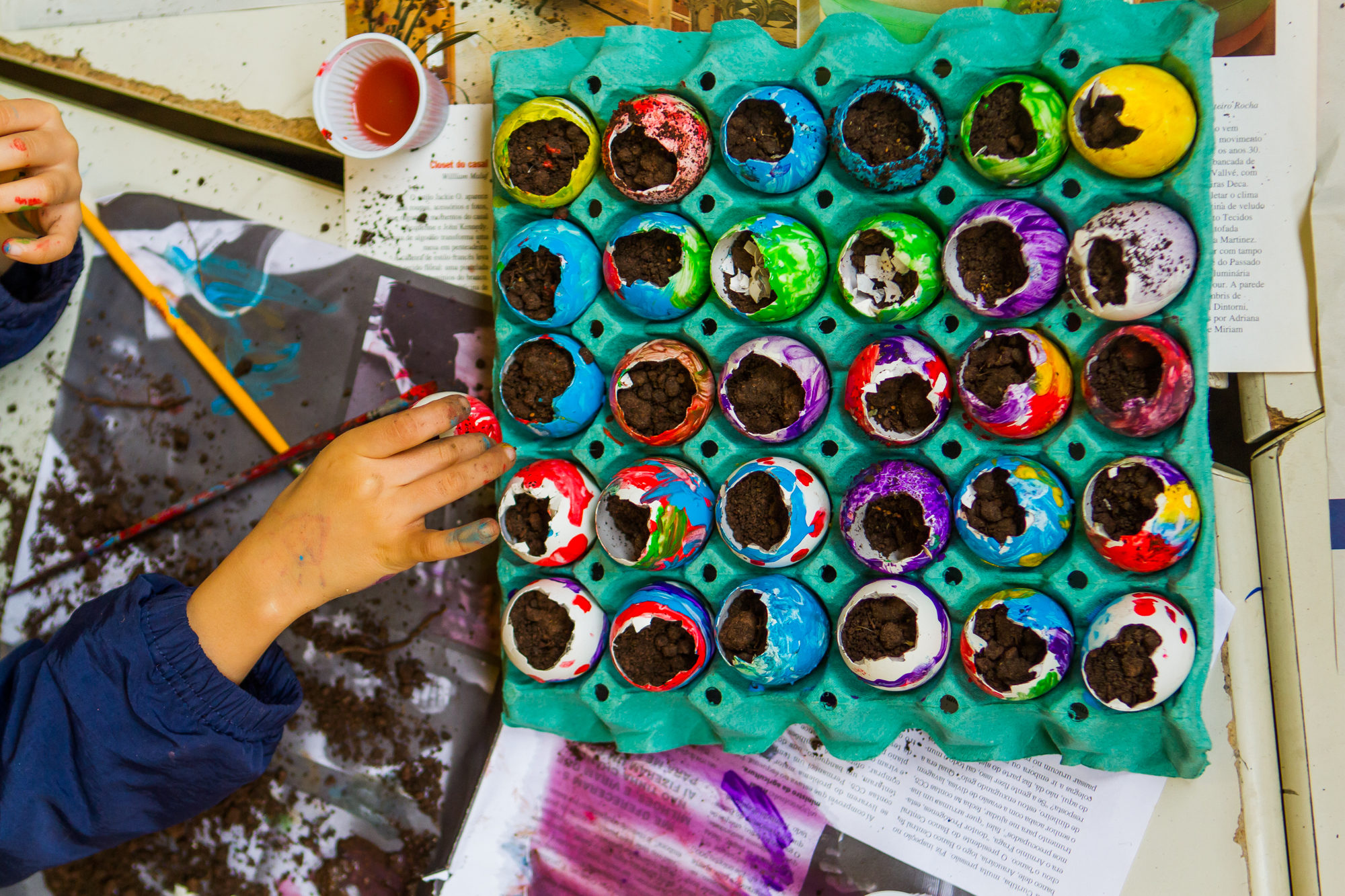 Na imagem, uma criança reutiliza cascas de ovos coloridas como vaso para plantinhas.
