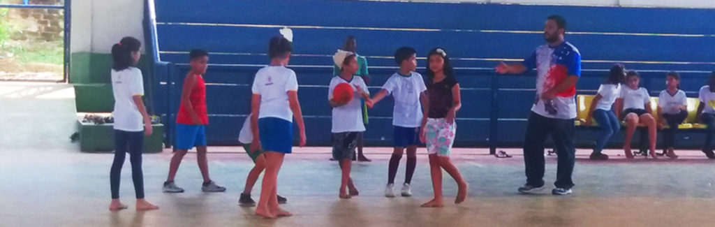 A fotografia mostra um grupo de crianças jogando bola na quadra da escola