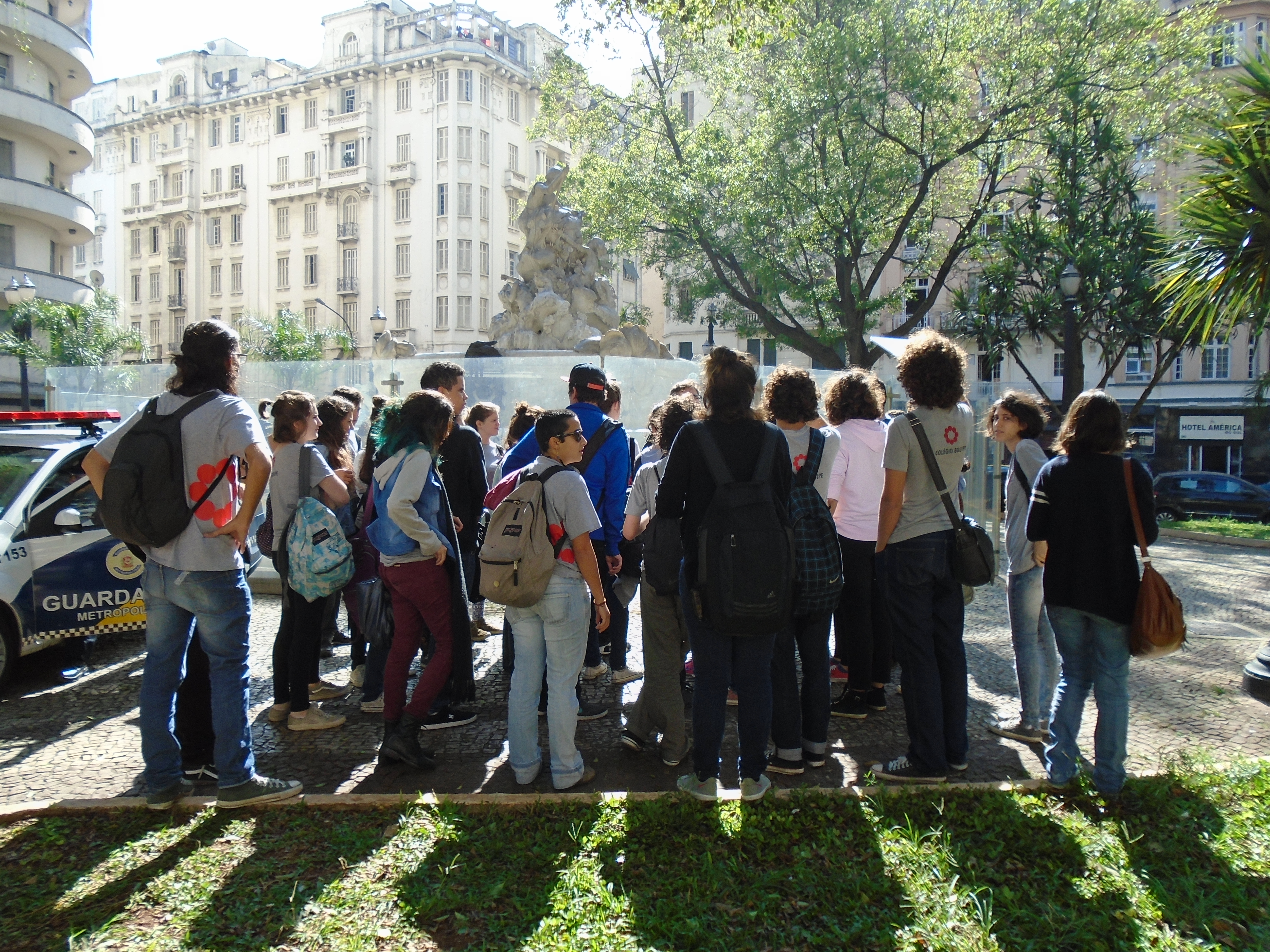 um grupo de estudantes estão parados, de costas para a câmera, observando um prédio