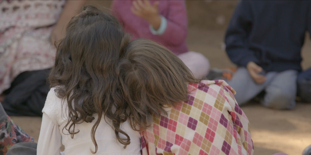 a imagem mostra duas crianças de costas sentadas lado a lado. Uma delas apoia a cabeça no ombro da outra.